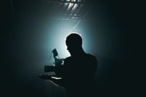 Silhouette of a cinematographer with camera gear in a dramatic, low light setting.